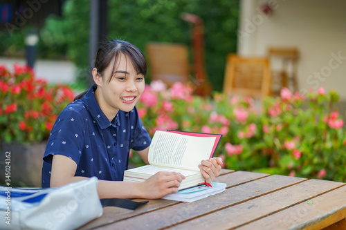 Young Asian student girl reading books while sitting at garden bench in home, education concept.