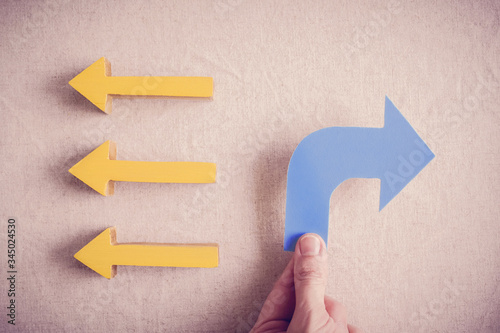 Quadro su tela Hands holding blue arrow to opposite direction of others, Disruptive innovation