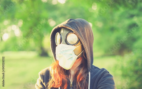 Woman wearing old hazmat style gas mask and medical mask, outside in bright summer environment.