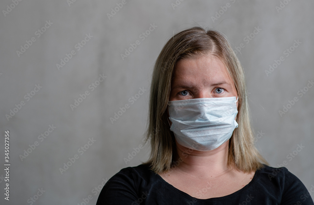 Woman wearing medical mask stands on gray background.  Pandemic coronavirus concept. Empty space for text
