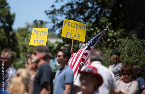 Crowd of people at Freedom Protest Rally during Covid-19 Stay-at-Home orders. Signs read FREEDOM over FEAR and American flag