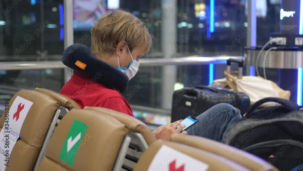 Man wearing medical face mask at the airport uses phone to prevent coronavirus infection during world epidemic