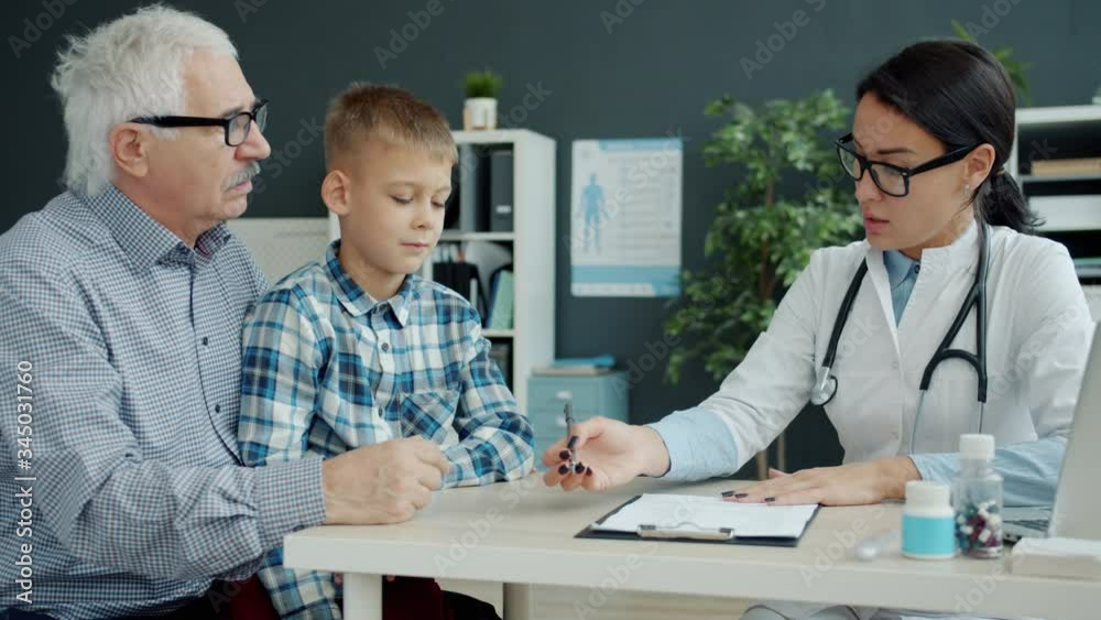 Female doctor is talking to caring grandfather and little grandson in office discussing child's health in hospital. Childhood, health and people concept. Female doctor is talking to caring grandfather and little grandson in office discussing child's health in hospital. Childhood, health and people concept.