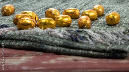 Chocolate eggs wrapped in golden paper arranged on green fabric symbolizing Easter Day