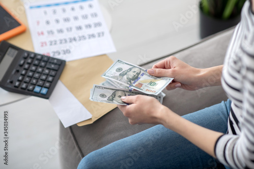 Female hands holding money notes near a calculator.