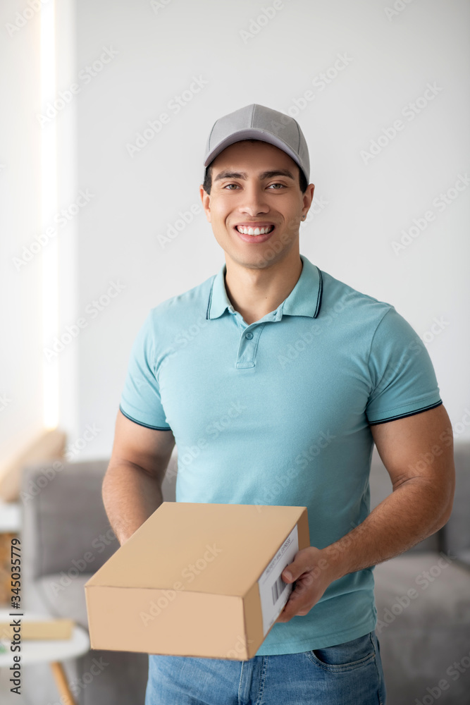 Brunette male courier holding brown cardboard box, smiling Brunette male courier holding brown cardboard box, smiling