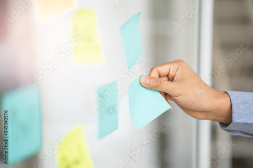 close up of asian businessman employee hand using and placing sticky note on glass board arranging mind map working in modern office, concept of planning, brainstorming business ideas and strategies