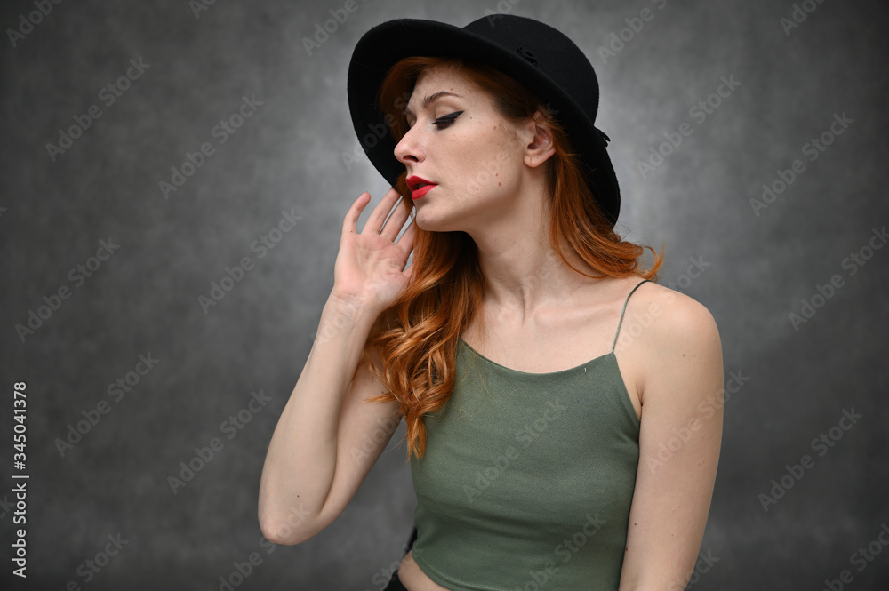 Woman shows emotions changing poses. Portrait of a young pretty girl with beautiful hair and great makeup in a green T-shirt and black hat on a gray background. Woman shows emotions changing poses. Portrait of a young pretty girl with beautiful hair and great makeup in a green T-shirt and black hat on a gray background.