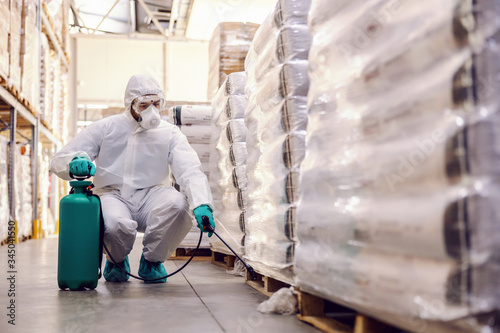 Man in protective suit and mask disinfecting warehouse full of food products from corona virus / covid-19. photo