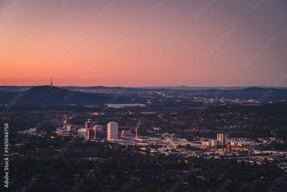 Aerial view overlooking a tiny city with buildings surrounded by landscape at sunset with orange colors on the horizon in the background
