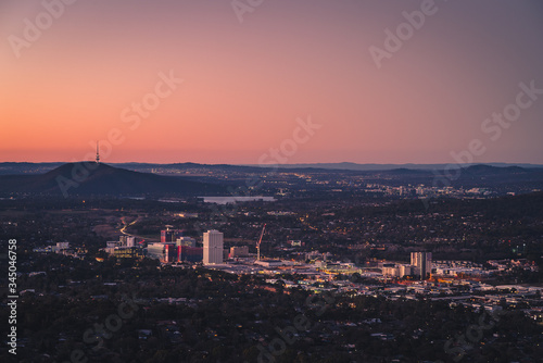 Aerial view overlooking a tiny city with buildings surrounded by landscape at sunset with orange colors on the horizon in the background © Matthew