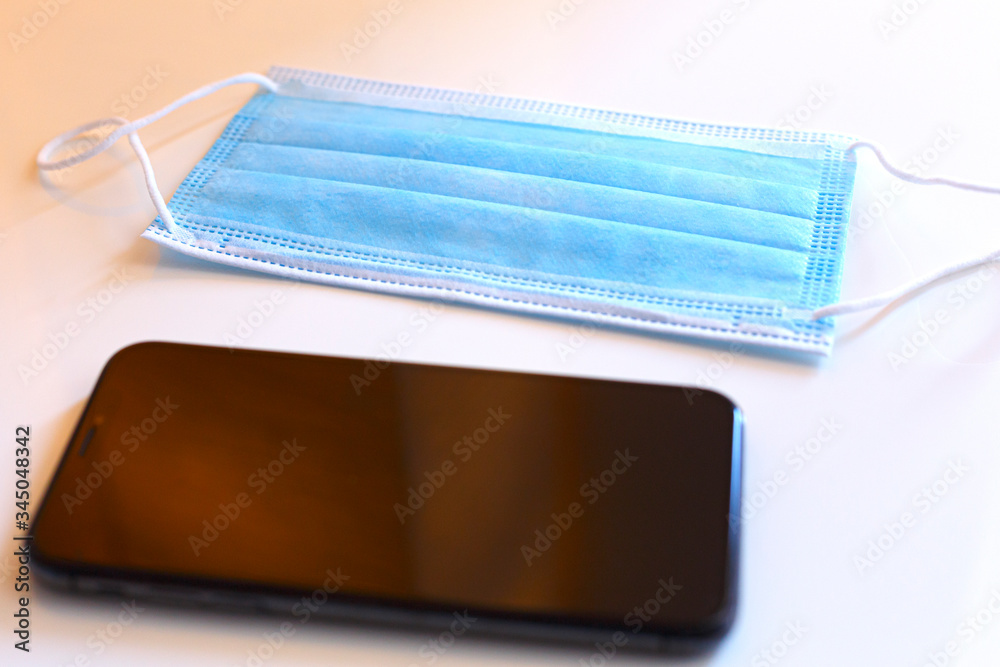 cellulare in primo piano con una mascherina chirurgica sullo sfondo , isolata su sfondo bianca