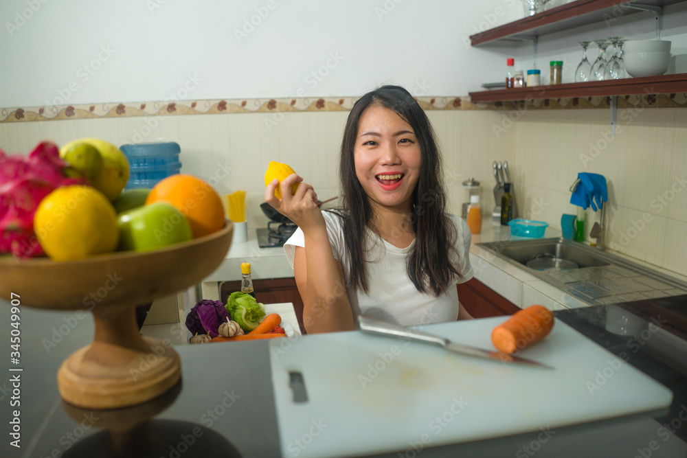 vegetable food and diet - home lifestyle portrait of young beautiful and happy Asian Chinese woman at domestic kitchen smiling cheerful in healthy nutrition and dieting concept