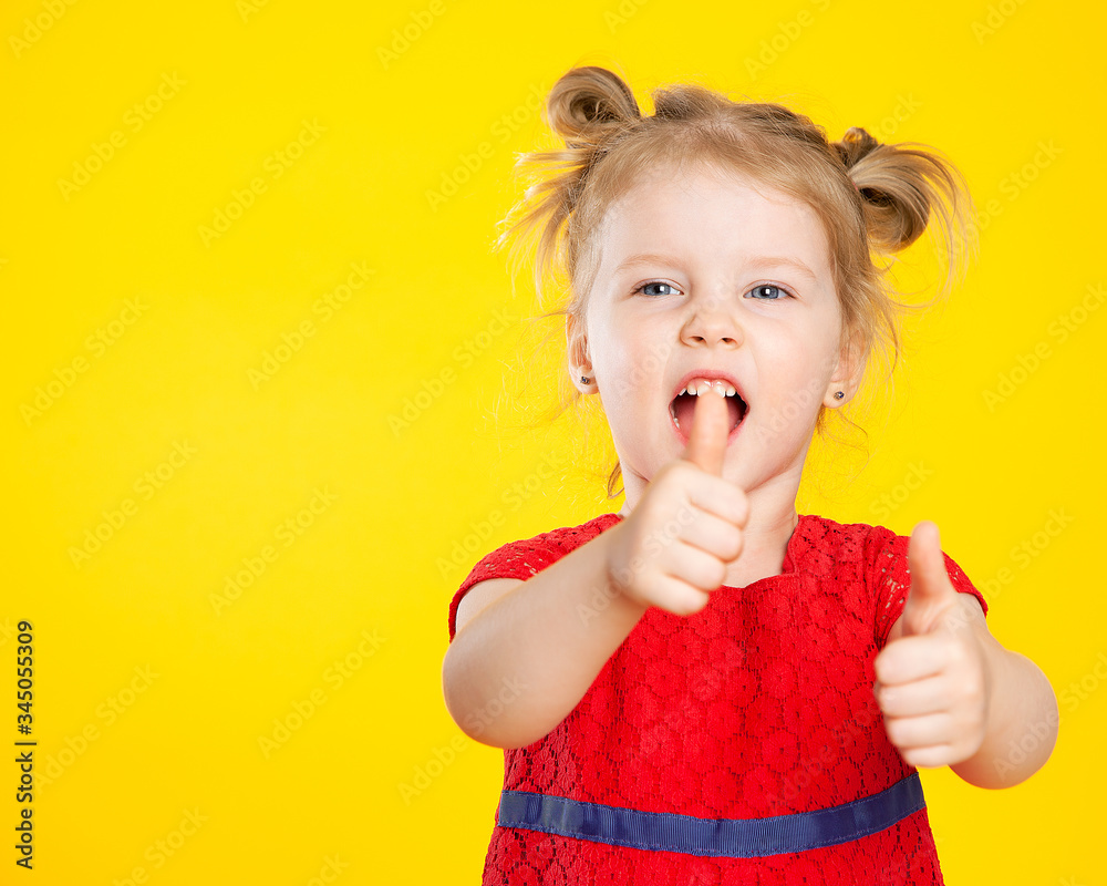 A small blonde European girl shows super, class and shouts, laughs. A child in a red dress on a yellow background. Funny, funny, crazy girl. Portrait of a happy child. Children's emotions. A small blonde European girl shows super, class and shouts, laughs. A child in a red dress on a yellow background. Funny, funny, crazy girl. Portrait of a happy child. Children's emotions.