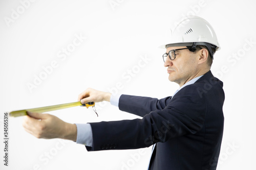 Handsome construction engineer in hard hat measures with tape measure on isolated white background. Construction, engineering tools, engineering and architecture concept photo