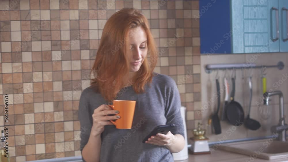 Redhead young girl drink coffee, taking selfie on phone. Portrait of happy hipster millennial girl in t-shirt making photo on smartphone. Smiling female posing with coffee on photo camera cellphone.