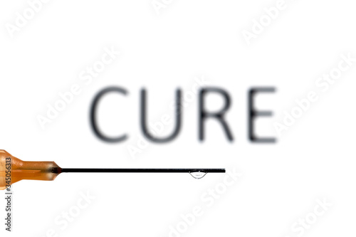 A medical needle with a droplet suspended refracting the word cure, which is also out of focus in the background
