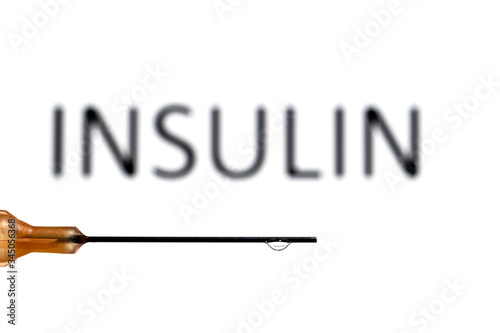 A medical needle with a droplet suspended refracting the word insulin, which is also out of focus in the background