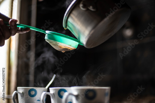 Tea being strained and poured into the cups from an aluminium tea pot in an Indian kitchen. Indian drink and beverages.