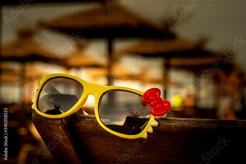 Warm summer. Sunglasses with a red bow are lying on the beach.
