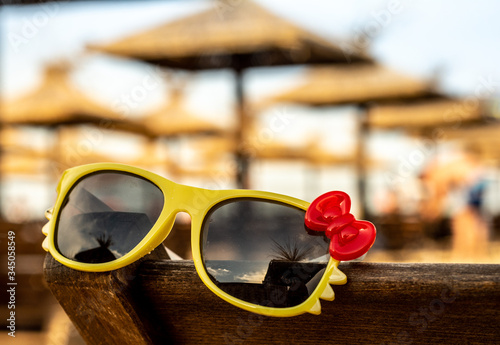 Warm summer. Sunglasses with a red bow are lying on the beach.
