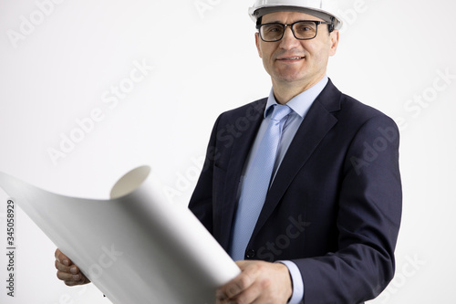 Portrait of handsome architect builder in protective helmet studying layout plan, smiling civil engineer working with documents isolated on white background. Successful man from industrial sphere photo