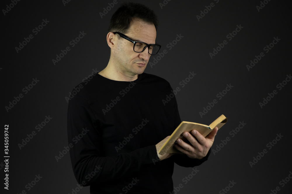 handsome casual dressed 40s man with dark hair in glasses closely reads book isolated on black background copy space concept writer and his book. reading pleasure concept bookstore advertising handsome casual dressed 40s man with dark hair in glasses closely reads book isolated on black background copy space concept writer and his book. reading pleasure concept bookstore advertising