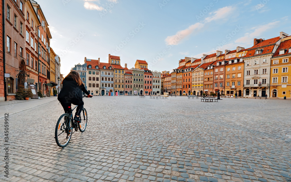 Woman on a bike rides on an empty Old Town Square in Warsaw, Poland - obrazy, fototapety, plakaty 