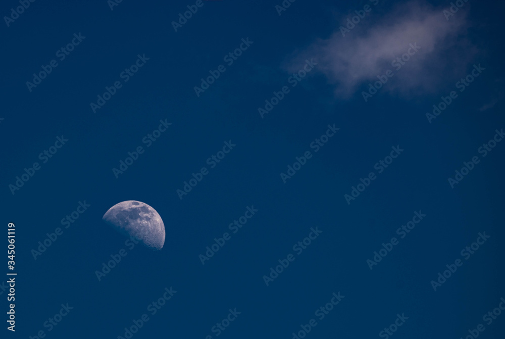 Daytime moon on a clear blue afternoon sky facing a small wispy cloud Daytime moon on a clear blue afternoon sky facing a small wispy cloud