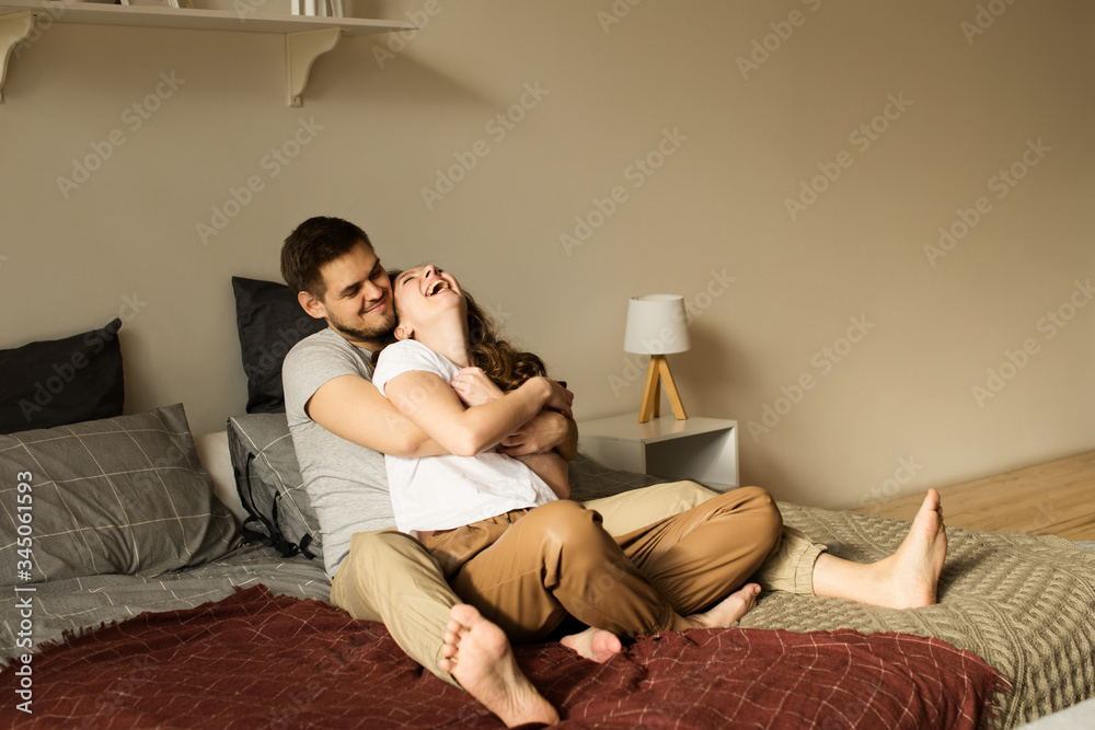 Couple young man and woman at home together, sitting on bed, hugs Couple young man and woman at home together, sitting on bed, hugs