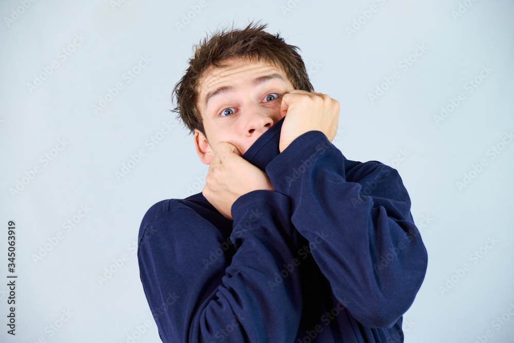 Scared handsome young man pulling up his blue sweater covering his mouth with a dramatic facial expression in the times of the corona pandemic. Scared handsome young man pulling up his blue sweater covering his mouth with a dramatic facial expression in the times of the corona pandemic.