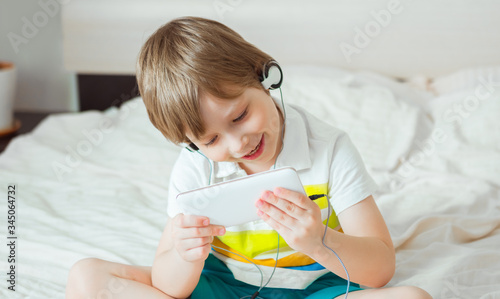 Modern little child sitting on bed with smartphone in his hands