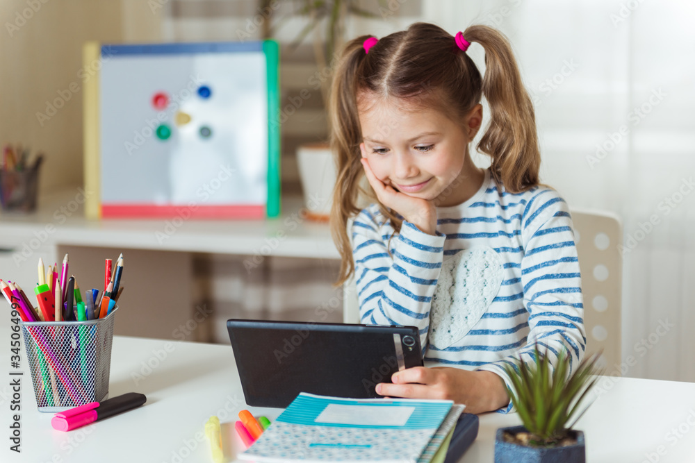 Distance learning online education. Smiling schoolgirl girl with digital tablet at home studying lessons. Online concept of school education and social distance during quarantine, self-isolation Distance learning online education. Smiling schoolgirl girl with digital tablet at home studying lessons. Online concept of school education and social distance during quarantine, self-isolation