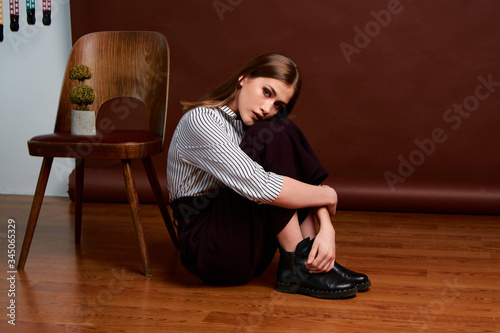 Gorgeous young female in classic suit, black shoes and grey coat. Vintage chair. Woman's clothes.