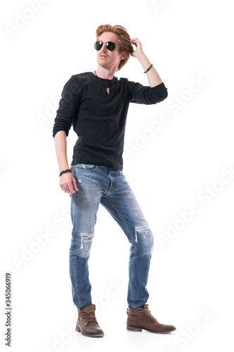 Handsome young red hair man with sunglasses turning back looking up over the shoulder touching hair. Full body isolated on white background. 