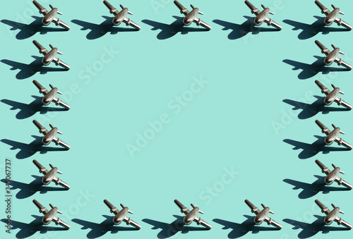 Frame of eigteen metal figures of small airplanes with shadows with the same space between them on the light mint color background. Conceptual geometric art trendy aviation boarder with empty space