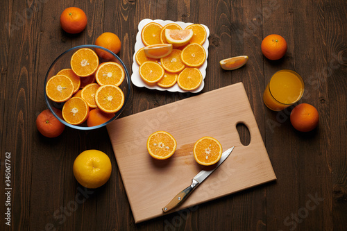 Fresh orange fruit whole and sliced on a wooden table, cutting board and kitchen knife. A plate full of citrus slices - natural and healthy food. Glass of fruit cocktail.