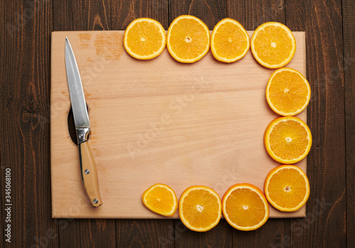 Fresh orange sliced fruits on a wooden table and cutting board with kitchen knife. Natural and healthy food. Arranged as a frame with blank space in center.