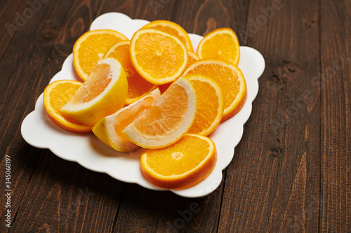 Fresh orange fruits sliced on a plate, dark wooden background - natural and healthy food.
