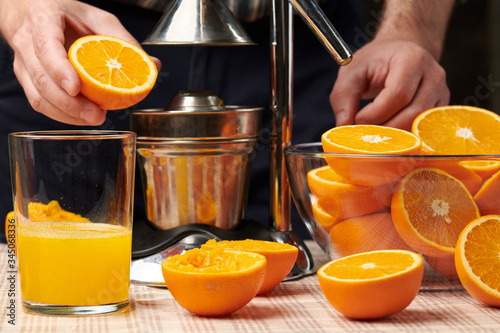 Squeezing an orange with a manual press, close view, making a glass of fresh. Fresh oranges on a wooden table, whole, squeezed and sliced.