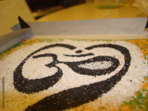 OM-the symbol of the universe. Om sound in yoga is used as a mantra. Sand painting. Close-up. Used black, white, yellow and green colors.Spiritual sign in Hinduism and Buddhism.