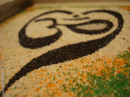 OM is a symbol of the universe. Om sound in yoga is used as a mantra. Sand painting. Close-up. Black, white, yellow and green colors. Harmony and spiritual practice.