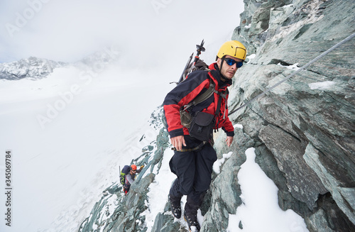 Vászonkép Full length of male mountaineer in sunglasses using fixed rope to climb winter mountain