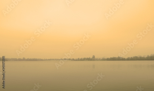 Yellow sunset over the lake in the fog