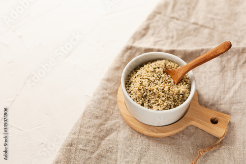 Cannabis kernels in a white bowl with a wooden spoon on a linen napkin on a white table