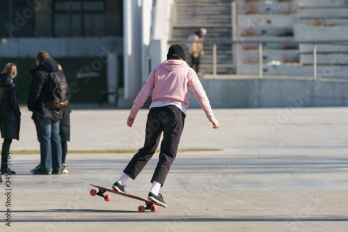 Young skateboarder performs a trick on a city street in sunny spring day. She is sliding. Back /rear view. Extreme sports is very popular among youth. Lifestyle during coronavirus pandemic
