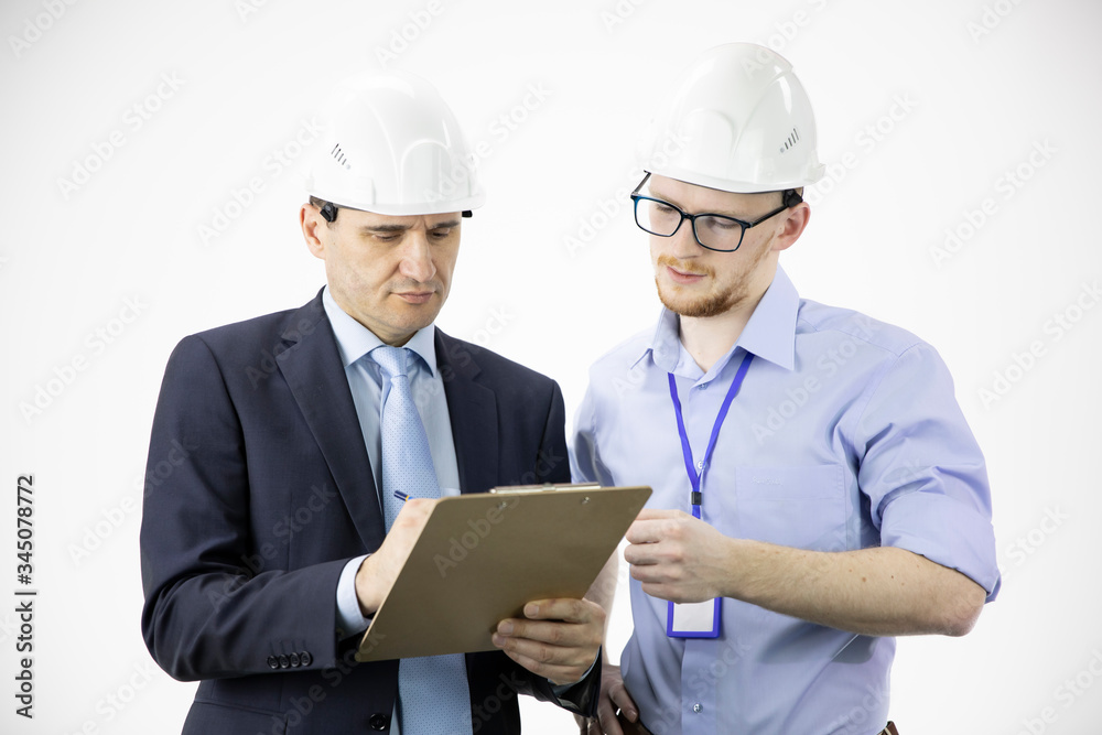Engineer and architect in hard hats discuss project while making notes in clipboard, calculating engineering decisions reading instructions, white background. Team work, BIM, Industry construction Engineer and architect in hard hats discuss project while making notes in clipboard, calculating engineering decisions reading instructions, white background. Team work, BIM, Industry construction