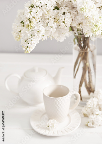 Bouquet of white lilac in vase and tea set on table in kitchen. Happy birthday greeting card. Hello spring and summer. Greeting card for Women's Day and Mother's Day. Spring season, copy space