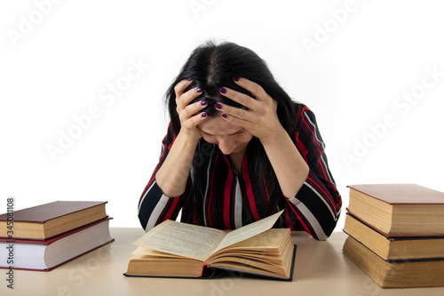 The young woman covered herself with a thick book. On the table are a bunch of thick books. Learns the text.