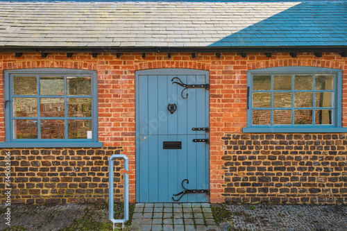 Small brick cottage in village in Southern England during Summer with Blue windows and wooden door